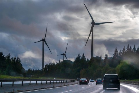 Tourist traffic on the A9 motorway during thunderstorms, wind turbines in the pine forest in the