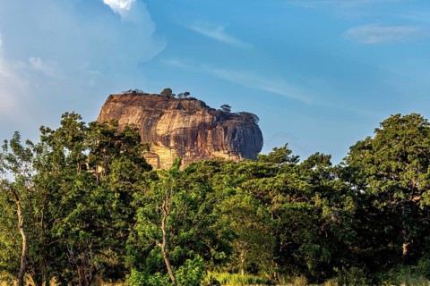 Large rock rises from a lush landscape with blue sky, The Lion Rock near Sigiriya in Sri Lanka
