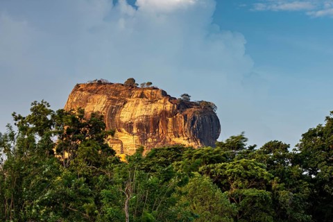 Massive rock juts out of the green landscape under a blue sky, The Lion Rock near Sigiriya in Sri