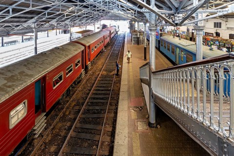 Station with red trains under a metal roof, people on the platform, The station and platform with