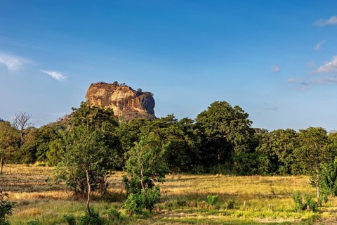 A rural view of a huge rock and lush meadows under clear skies, The Lion Rock near Sigiriya in Sri