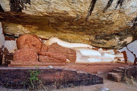 Ancient sandstone sculpture of a Buddha reclining under a rocky outcrop, tranquil setting, The