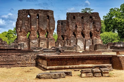 Brick ruins rising up against the sky surrounded by green foliage and crumbling architecture, The