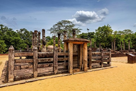 Wooden gate flanked by stone pillars on a sandy floor under a cloudy sky, The temples of