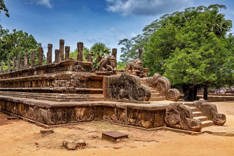 Stone wall with engraved sculptures and stairs surrounded by tall trees, The temples of Polonnaruwa