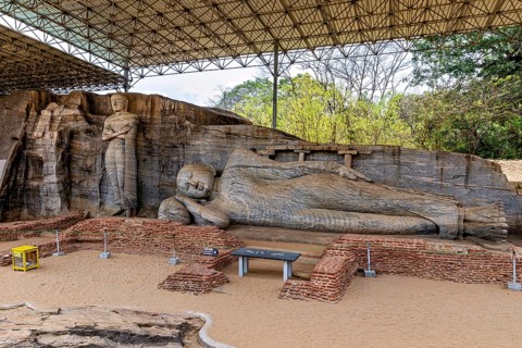 Panoramic view of a large reclining Buddha statue with a figure standing next to it under a