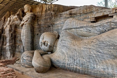 Close-up of the artistic detail of a large reclining Buddha statue next to a standing figure carved