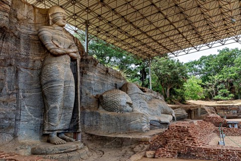 Monumental rock statue with standing and resting figure under a canopy surrounded by nature and