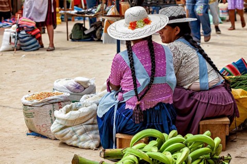Two woman wearing hats and traditional dresses discuss their market status, The Rurrenabaque market