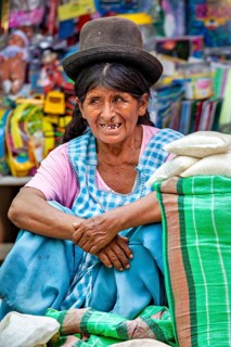 A woman in traditional clothing and hat sits quietly at a market, the Rurrenabaque market in