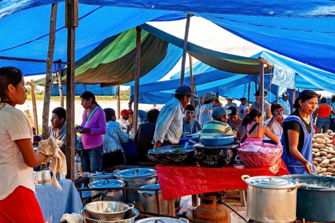 People cook and serve food under blue tarps in a busy market atmosphere, The Rurrenabaque market in