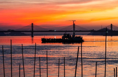 A boat sails on the river Brahmaputra during sunset, with the silhouette of a cable-stayed bridge
