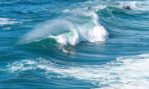 Surfers with their jet ski pilots in the Atlantic waves below Farol de Nazaré, Forte São Miguel,