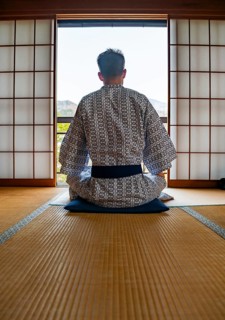 Young man wearing kimono sitting in traditional Japanese living room with tatami mats and shoji