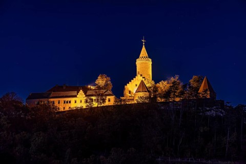 Illuminated castle at night, on a hill, surrounded by shadows and a bright blue night sky, The