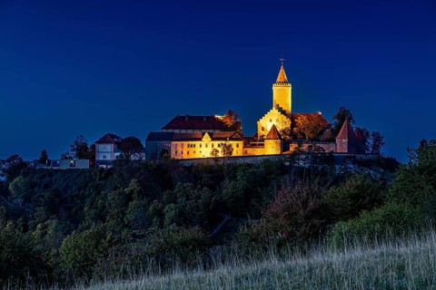 A castle at dusk, illuminated and picturesquely situated on a hill, in contrast to a clear blue