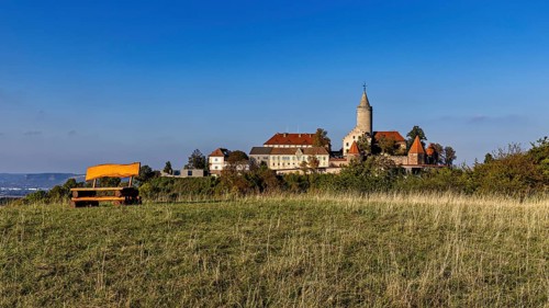 A castle on a hill with a wide meadow in the foreground and clear blue sky, The Leuchtenburg near