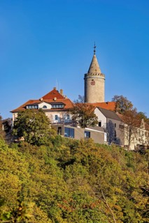 A castle with a distinctive tower, surrounded by colorful autumn trees against a clear sky, The