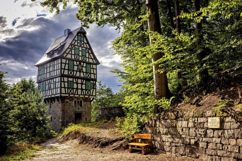 Half-timbered house in the forest, next to a paved path and a wooden bench, under sunlight with