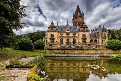 Castle with dramatic architecture reflected in a quiet pond surrounded by nature, The Hummelshain