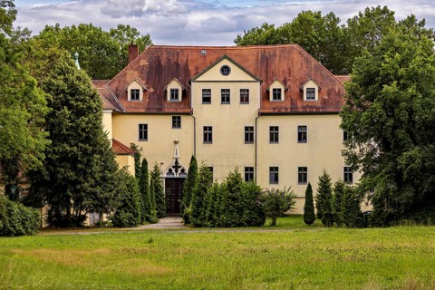 Yellow castle with distinctive roof and well-kept garden surrounded by trees, The Hummelshain