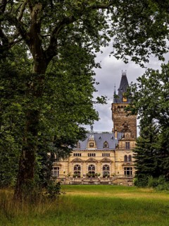 A castle with a high tower, nestled in thick trees, under cloudy skies, The Hummelshain hunting