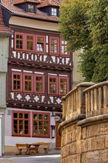 A half-timbered house with red window frames next to a stone wall in a historic town, The old town