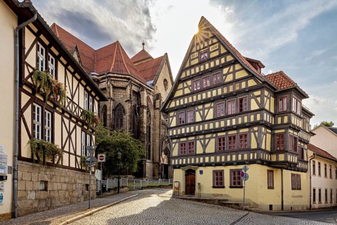 Sun-drenched street with half-timbered house and church, quiet atmosphere and clear architecture,