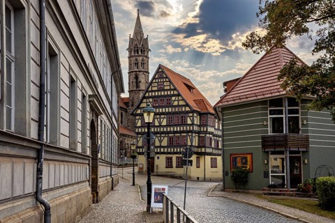 Paved street with half-timbered houses and church tower under a cloudy sky, the old town of