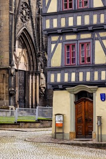 Detailed view of a church portal next to a half-timbered house, paved street in front of it, the