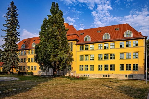 Yellow historic building with red roof, surrounded by trees and summer atmosphere, The old town of