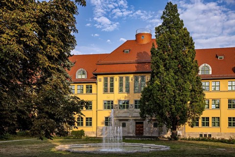 Large yellow building with surrounding garden, fountain and summer backdrop, the old town of