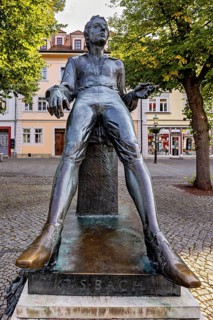 Statue of a smiling man in a square with buildings, Johann Sebastian Bach monument in the old town