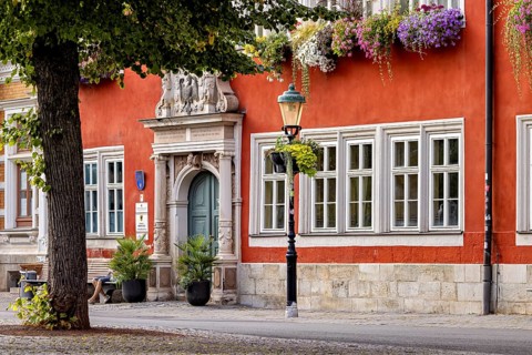 Red façade with blooming flowers and lantern next to an ornate entrance in the old town, The old