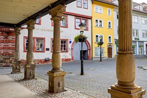 Columns in the city center surrounded by brightly painted historic buildings on cobblestones, The