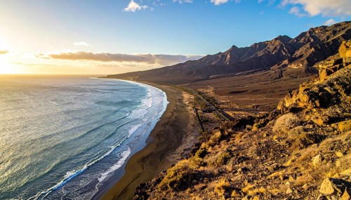 Desert landscape converges with ocean along a rugged coastal area, shore break at cliffs, blue