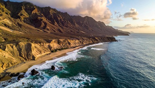 Desert landscape converges with ocean along a rugged coastal area, shore break at cliffs, blue