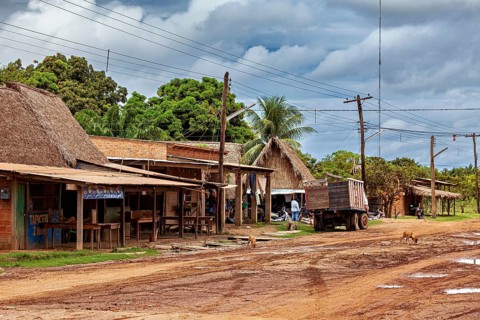 Rural scene with thatched buildings and a lorry on a muddy village road under a cloudy sky, houses