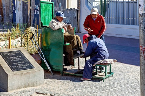 Three men interact in a relaxed street scene at a shoe shiner in the old town, show shiners in the