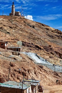 Church on a mountain in a barren, dry landscape with antennas and stone houses under a blue sky,