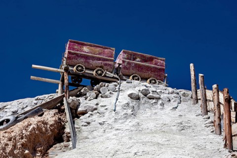 Two old mine cars standing on a rocky structure above a stony slope under a clear sky, mining lore