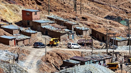 Several clay-coloured houses in a mountainous landscape with parked cars and rubble, The silver
