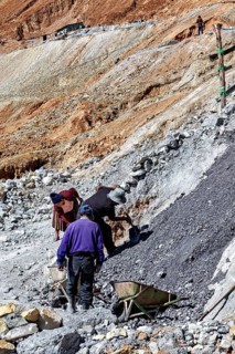 Workers bend on a rocky slope while loading gravel into wheelbarrows, The silver mines of Potosi