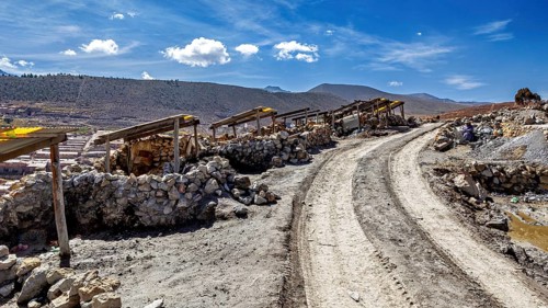 Dusty path with piles of stones next to a mountainous landscape under a blue sky with clouds, The