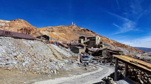 Old industrial complex in a mountainous environment under a clear blue sky with a visible path, The