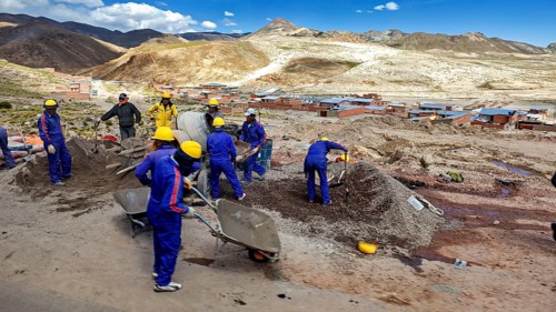 Workers in blue work clothes shovel earth on a sunny hilly landscape, surrounded by mountains and