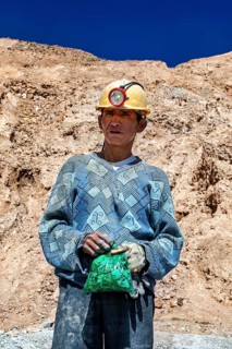 A man in a helmet and patterned jumper stands in front of a rocky landscape, The miners of the
