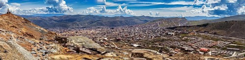 Expansive panorama of an urban landscape embedded in mountainous surroundings under a blue sky,
