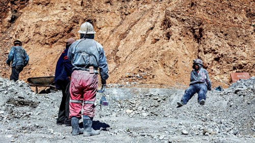 Miners in different clothes stand or sit in a barren, dusty environment, The miners of the Cerro