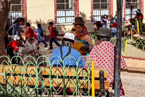 Women in traditional dress sit in the park while children play, people of the town of Uyuni in the